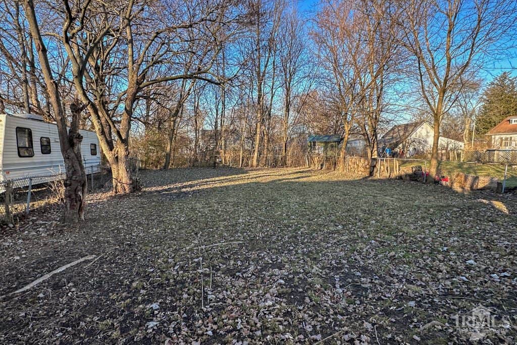 Large backyard in Muncie, Indiana, perfect for outdoor activities, with mature trees, fencing, and neighboring homes.